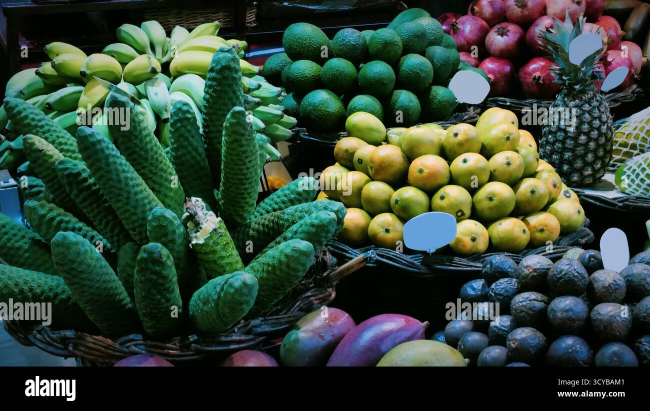 Colorato mercato di frutta tropicale con cesti di manghi, banane, cherimoya, avocado e agrumi. Esposizione di prodotti freschi con etichette dei prezzi. Ideale per chi ama Foto Stock