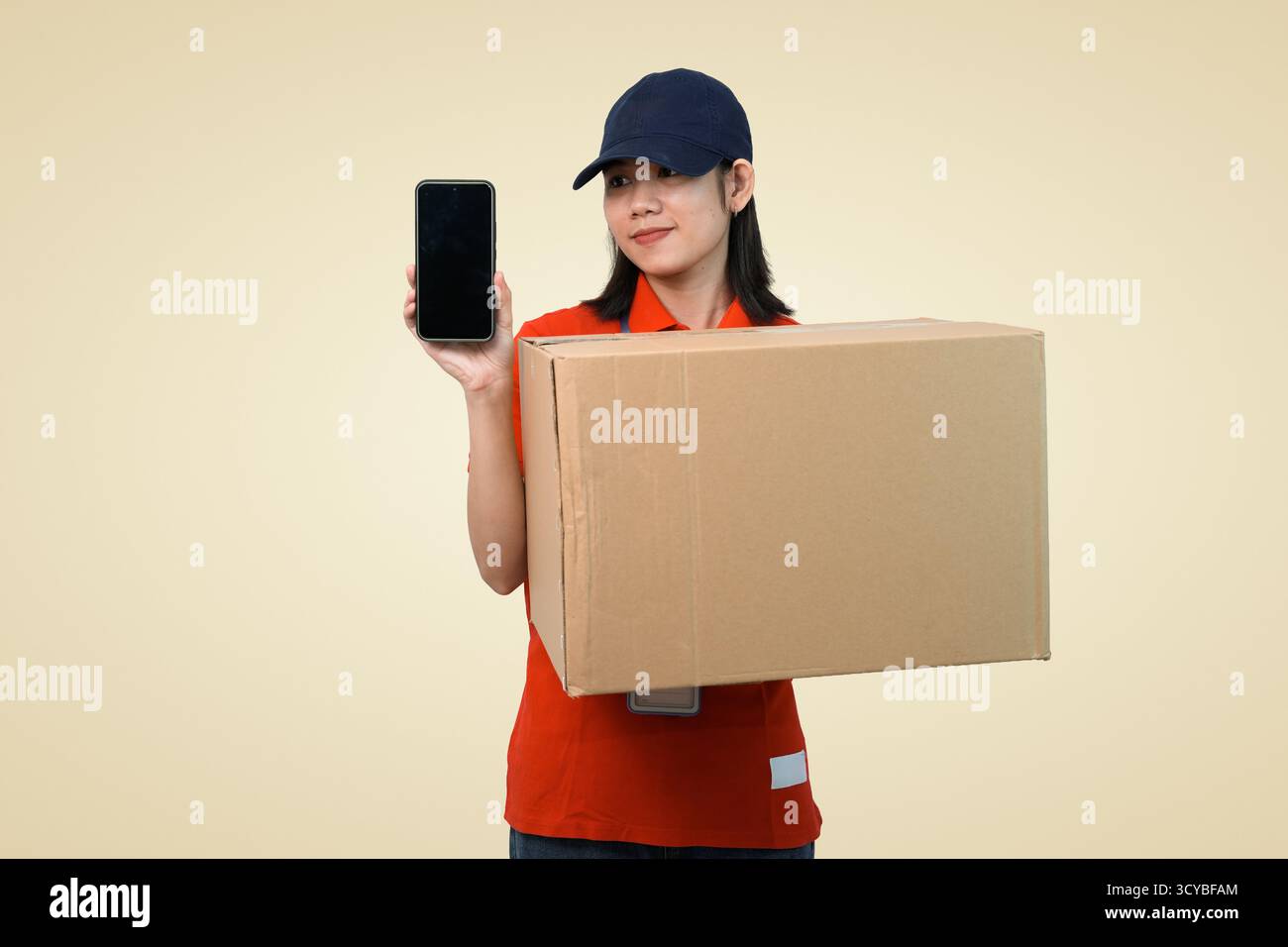 consegna giovane lavoratore con espositore per smartphone e confezione, corriere sorridente pronto per la consegna a casa in studio Foto Stock