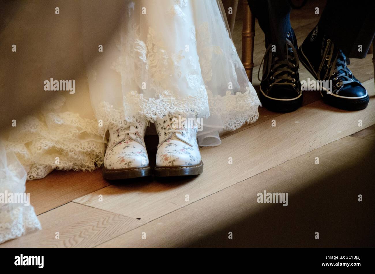 Un moderno dettaglio di nozze che cattura le eleganti sneakers floreali della sposa accanto alle sneakers casual nere dello sposo, unendo stile e personalità Foto Stock