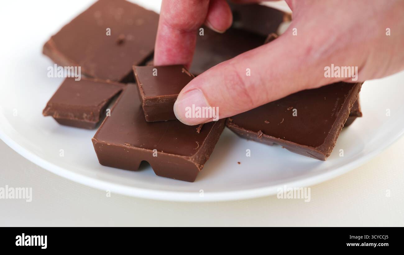Un uomo che prende un pezzo di cioccolato al latte rotto da un piatto. Primo piano. Foto Stock