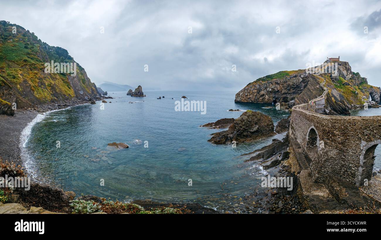 Storico ponte in pietra e hermitage sull'isolotto roccioso nella baia di Gaztelugatxe con le spettacolari scogliere costiere. Simbolo basco Foto Stock