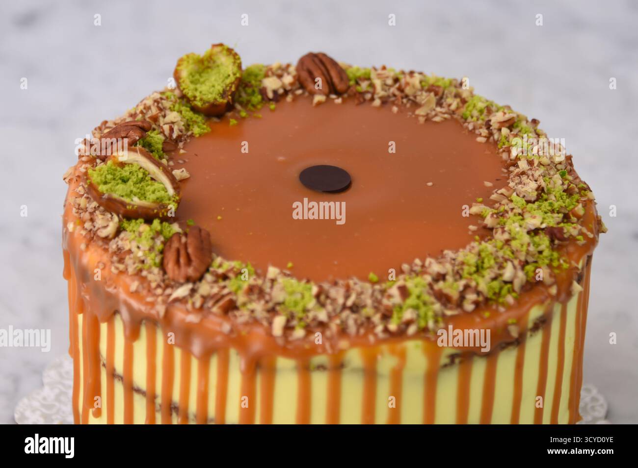Torta al caramello al pistacchio con strati di torta umida condita con ricco caramello, ricoperta da pistacchi tritati e metà di noci pecan su fondo grigio Foto Stock
