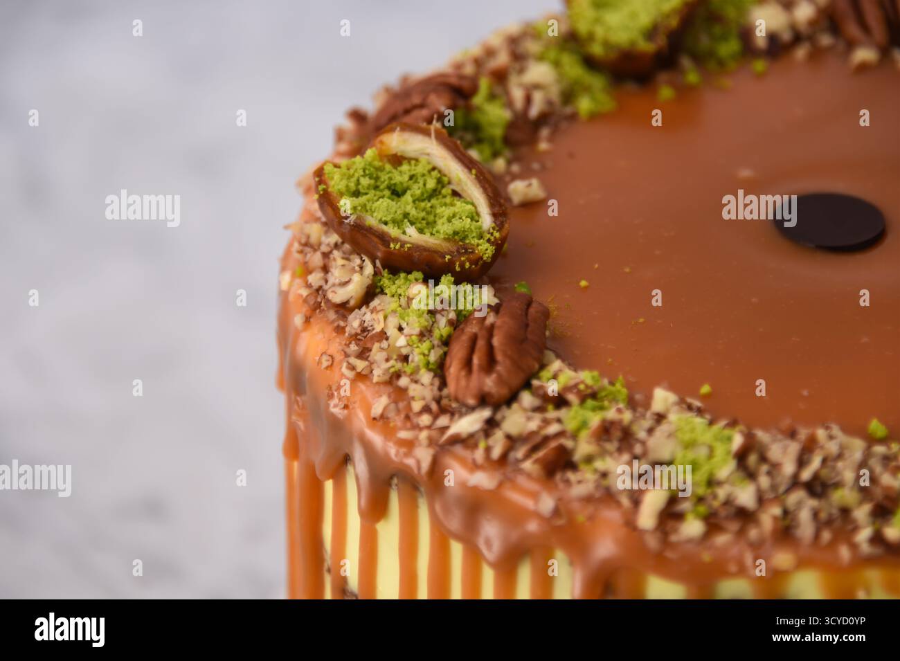 Torta al caramello al pistacchio con strati di torta umida condita con ricco caramello, ricoperta da pistacchi tritati e metà di noci pecan su fondo grigio Foto Stock
