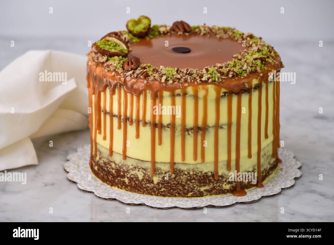 Torta al caramello al pistacchio con strati di torta umida condita con caramello ricco, ricoperta di pistacchi tritati e metà di noci pecan con tovagliolo Foto Stock