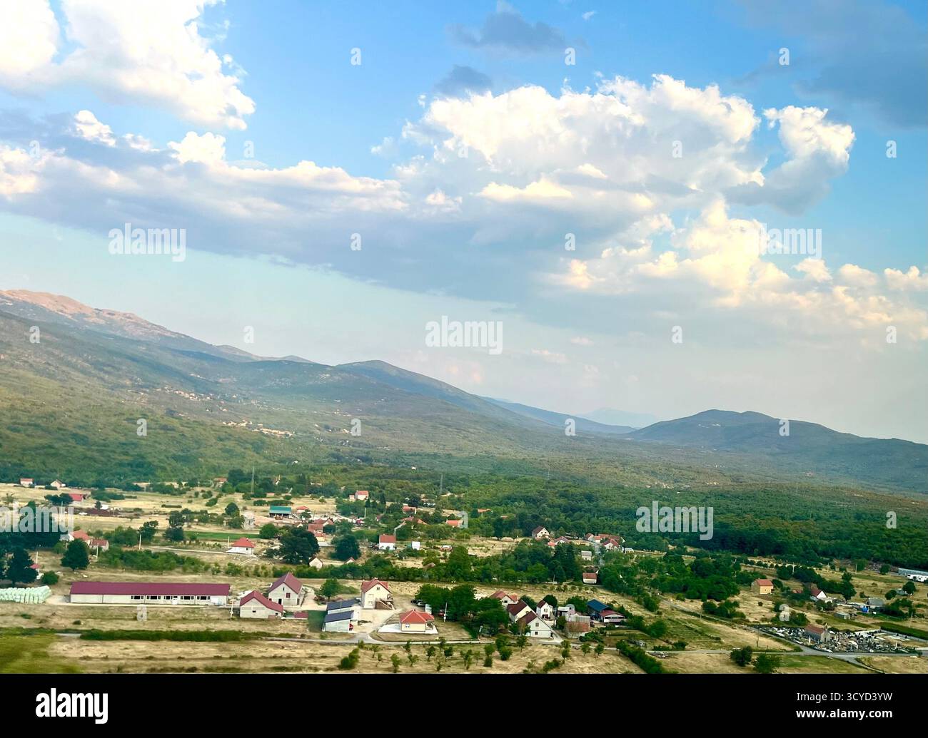 Tranquilla valle rurale con piccole case, colline verdi e cielo azzurro nuvoloso, ideale per viaggi, natura e temi di campagna. - Immagine stock catturata con smartphone