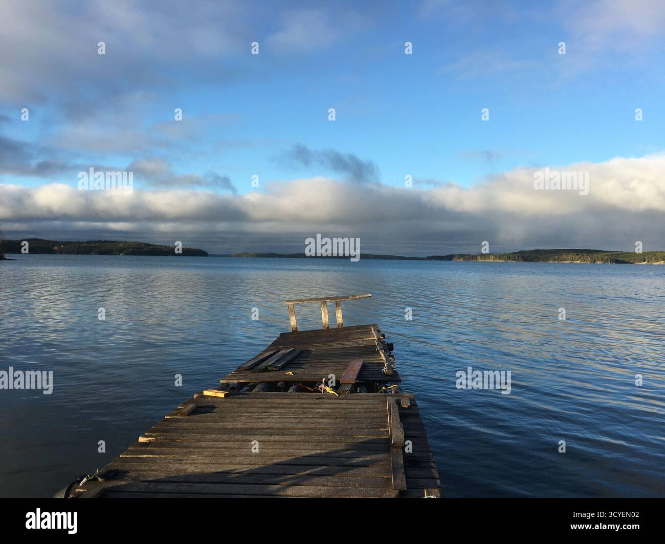 Tranquillo molo in legno che si estende su un tranquillo lago sotto un cielo parzialmente nuvoloso, offrendo un tranquillo rifugio sul lago. Foto Stock