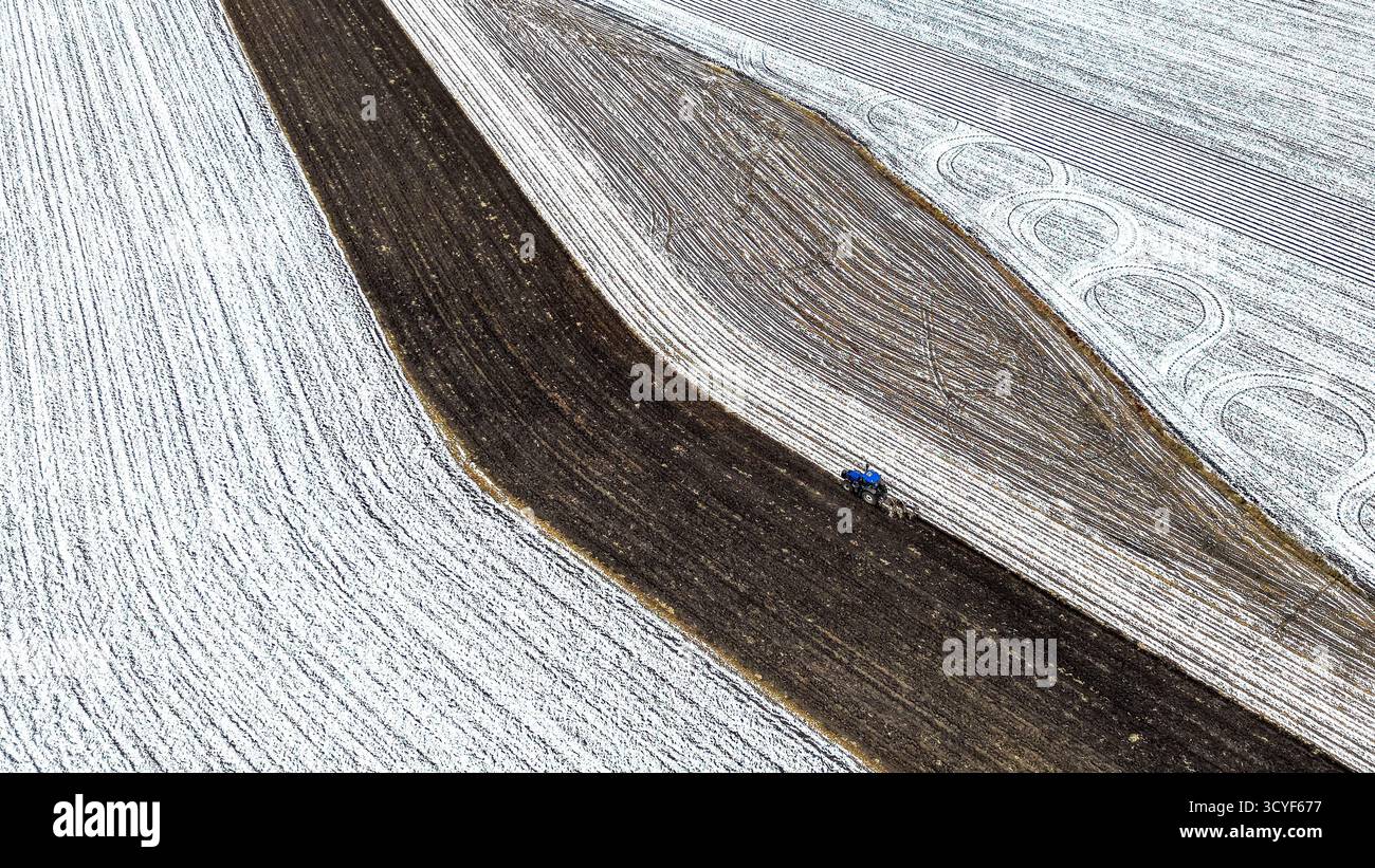 Pechino, Cina. 18 ottobre 2025. Una foto aerea scattata il 18 ottobre 2025 mostra una macchina agricola che lavora in un campo innevato di un'azienda agricola sotto il gruppo Beidahuang nella provincia di Heilongjiang della Cina nord-orientale. Poiché molte aree della provincia di Heilongjiang hanno subito nevicate, alcune unità di produzione agricola del gruppo Beidahuang hanno preparato il terreno per l'inverno prima che il terreno si congeli. Crediti: Huang Yongxing/Xinhua/Alamy Live News Foto Stock