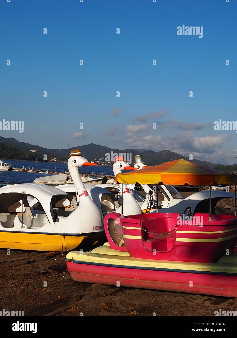 Le barche dei cigni si allinearono sulla riva del lago Yamanaka in autunno, nella prefettura di Yamanashi, in Giappone, sotto un cielo azzurro e cristallino con sfondo montano Foto Stock