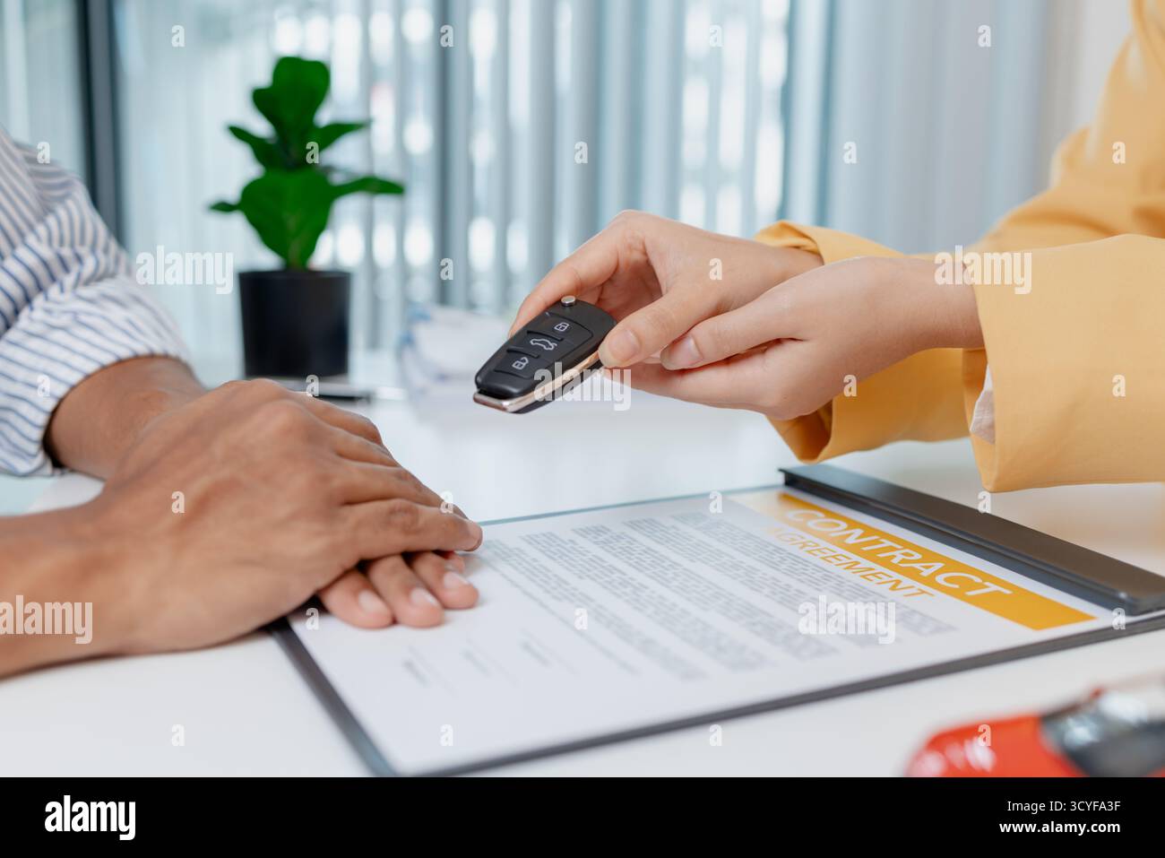 Una negoziazione per la vendita di auto si svolge in un ufficio in cui una donna venditrice con un blazer giallo spiega i dettagli di un contratto a un cliente maschio, showin Foto Stock