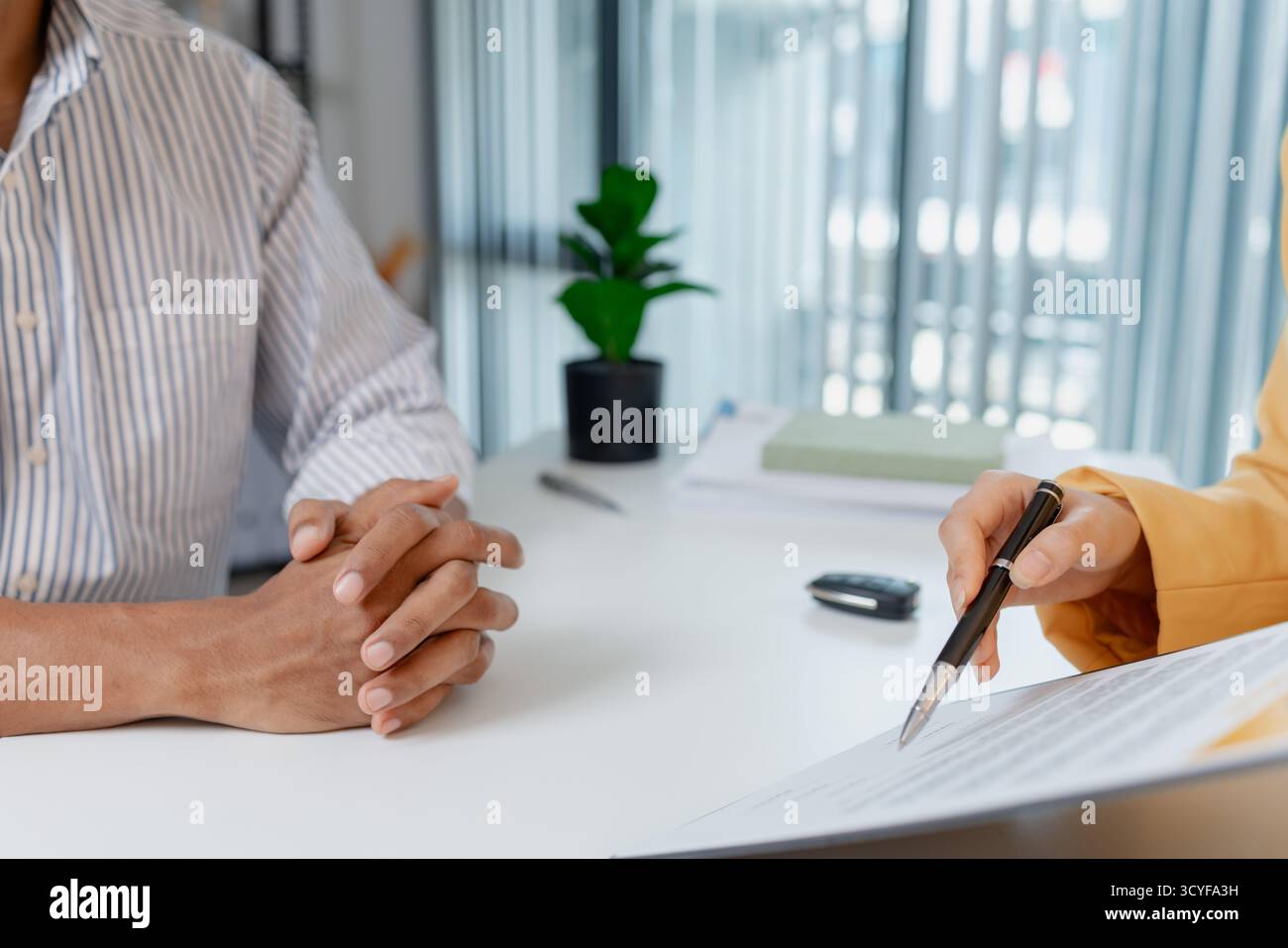 Una negoziazione per la vendita di auto si svolge in un ufficio in cui una donna venditrice con un blazer giallo spiega i dettagli di un contratto a un cliente maschio, showin Foto Stock
