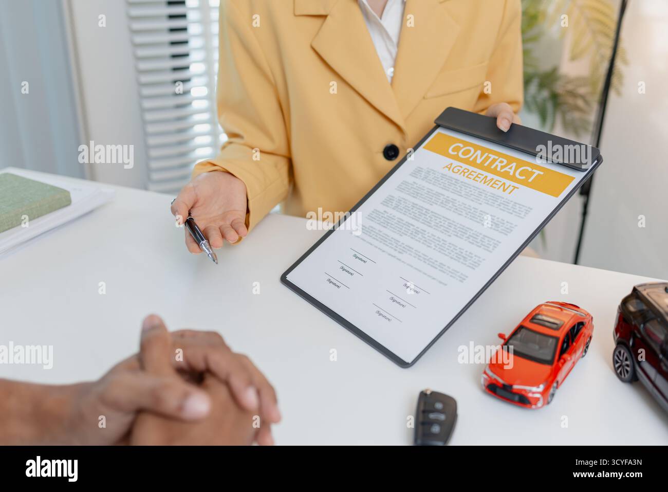 Una negoziazione per la vendita di auto si svolge in un ufficio in cui una donna venditrice con un blazer giallo spiega i dettagli di un contratto a un cliente maschio, showin Foto Stock