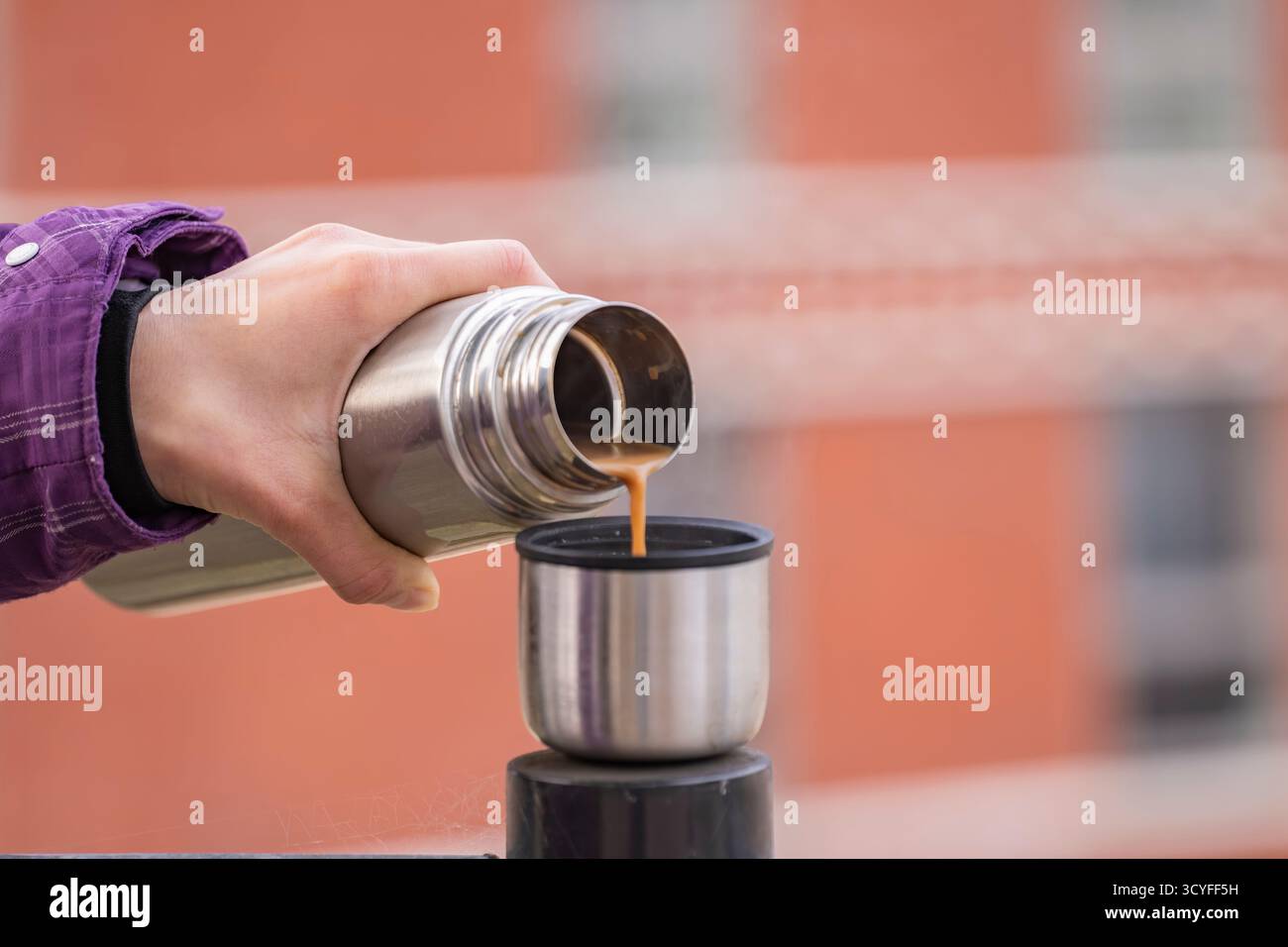 Versare a mano caffè caldo da Thermos nella tazza - foto per esterni con vista laterale su sfondo rosso della parete Foto Stock
