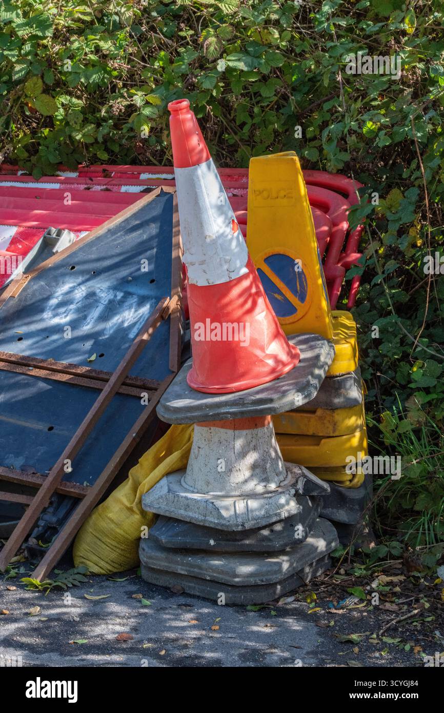 un mucchio di cartelli segnaletici, dissuasori, coni stradali e barriere lasciate sul ciglio della strada dopo il completamento dei lavori stradali, cartelli dei lavoratori stradali lasciati in un mucchio di strada. Foto Stock