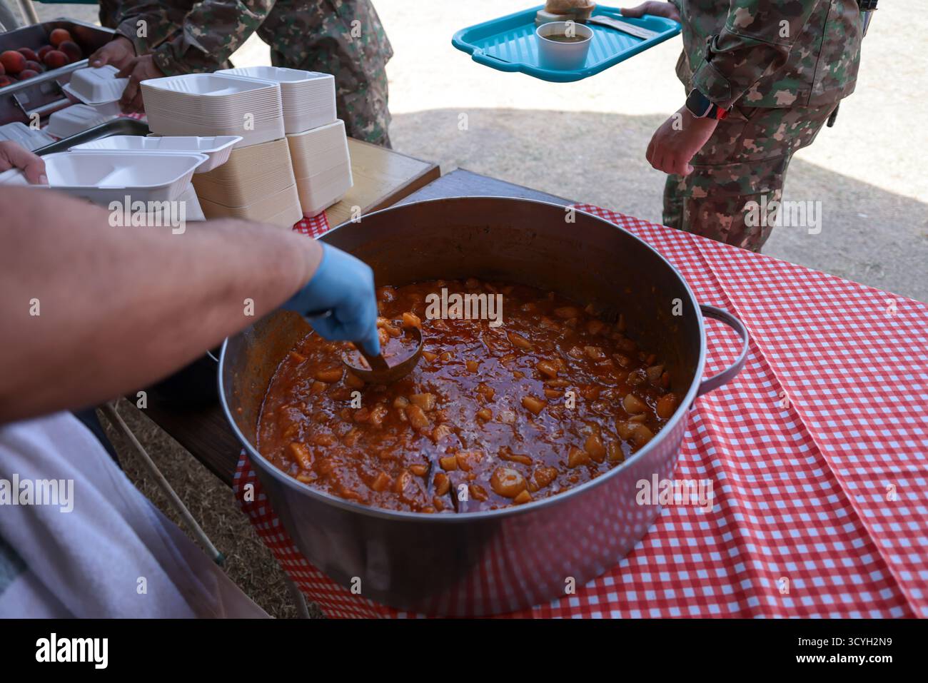 Dettagli con le mani di una persona che serve il personale dell'esercito rumeno con il cibo da una grande pentola da cucina. Foto Stock