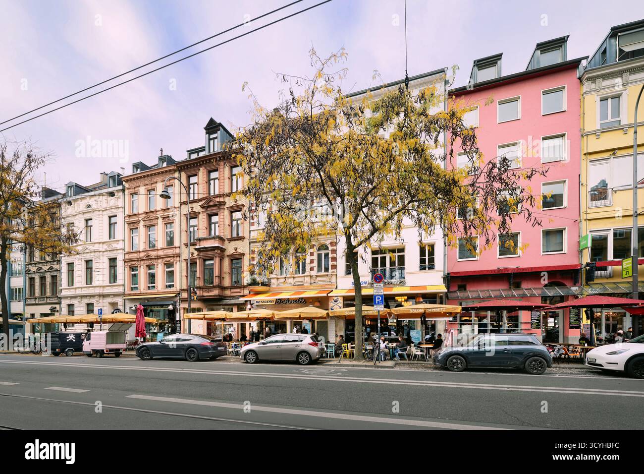 Aachener Straße a Colonia in ottobre. Edifici storici, caffetterie di strada con albari e alberi autunnali in Una giornata nuvolosa nell'ottobre 2025 Foto Stock