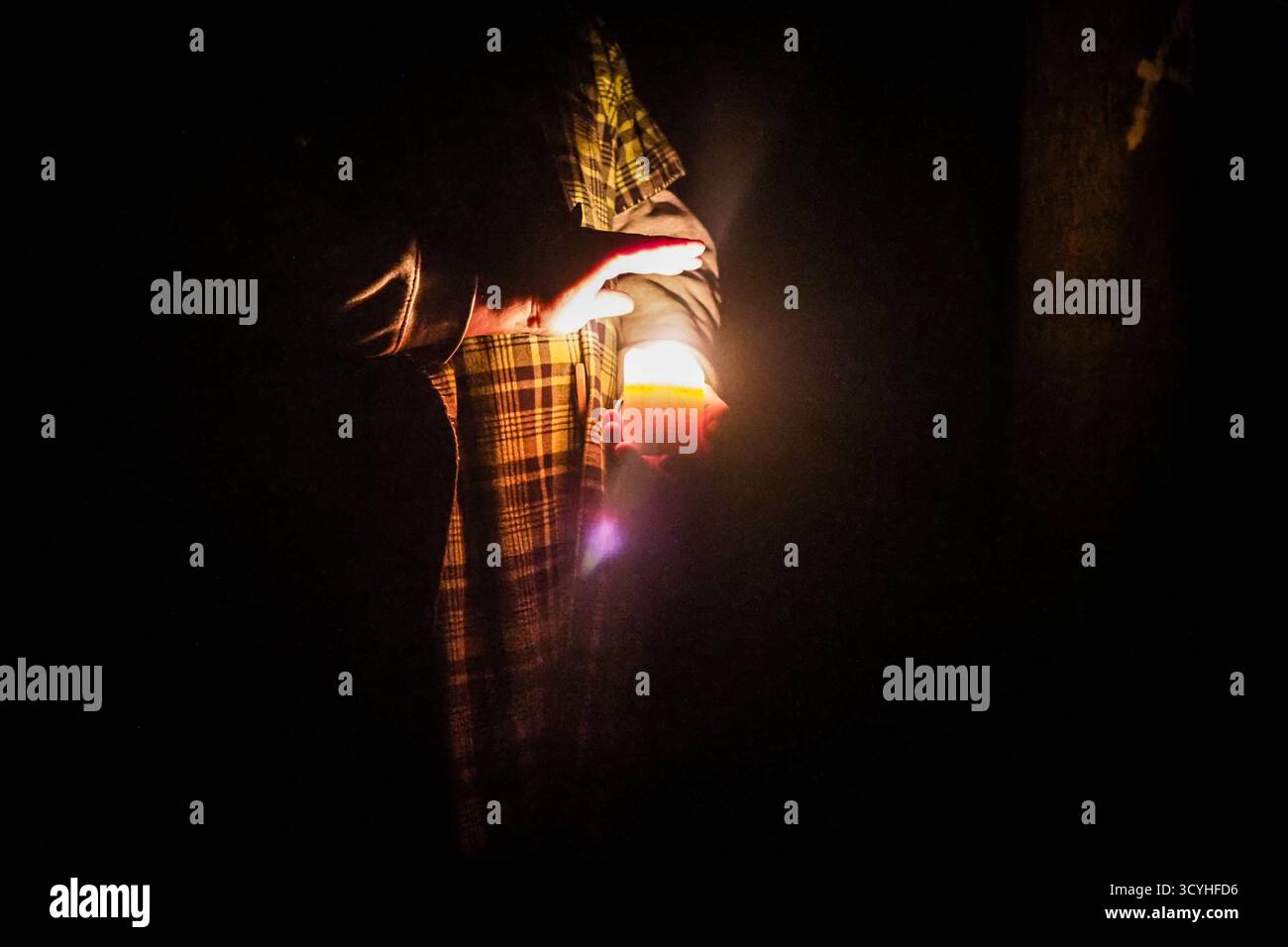 Persona che tiene in mano una candela al buio, luce che si riflette sulle mani e sui vestiti in una scena notturna con scarsa illuminazione. Foto Stock