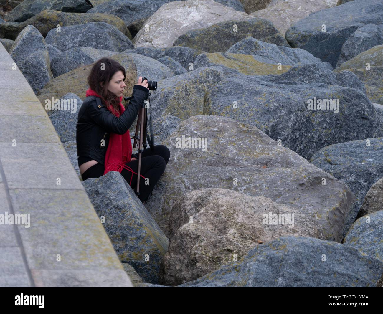 Fotografa donna con fotocamera e treppiede tra le rocce costiere Foto Stock