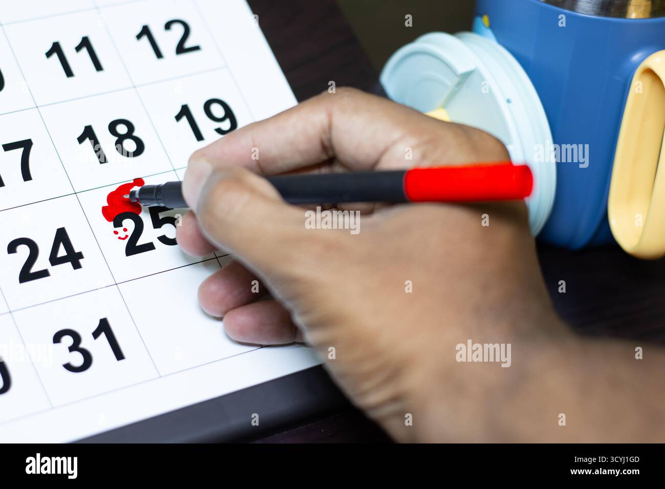 Uomini che fanno uno sforzo gioioso per celebrare il natale disegnando il cappello rosso di babbo natale nel calendario che è segnato il 25 per celebrare il natale. Foto Stock