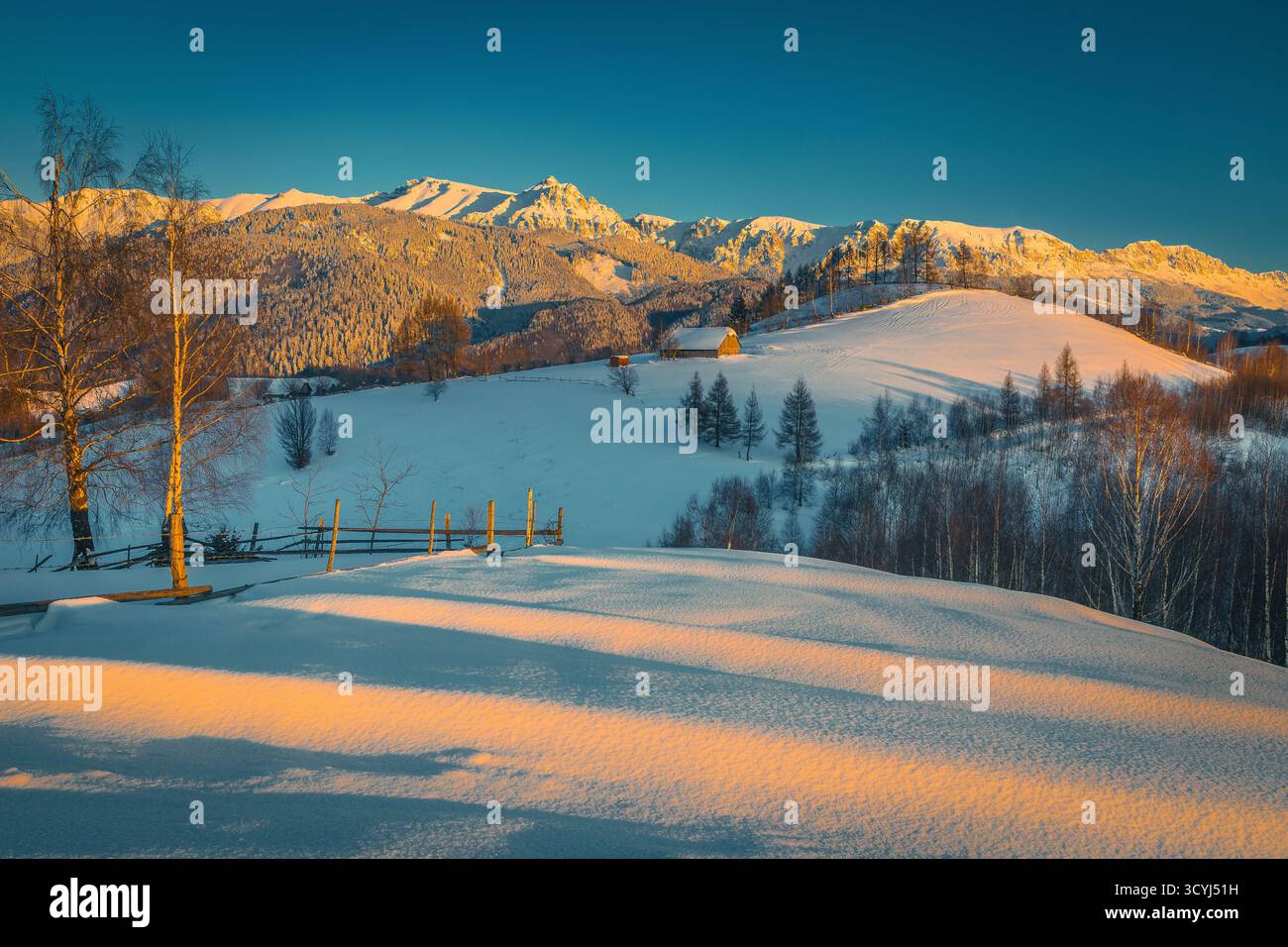 Pittoresco paesaggio invernale con colline innevate e splendide alte montagne sullo sfondo al tramonto, montagne Bucegi, Carpazi, Romania, EUR Foto Stock