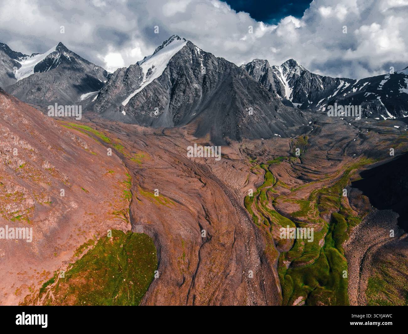 Vista panoramica aerea di una massiccia morena glaciale erosa con motivi marroni e verdi che portano a torreggianti montagne innevate Foto Stock