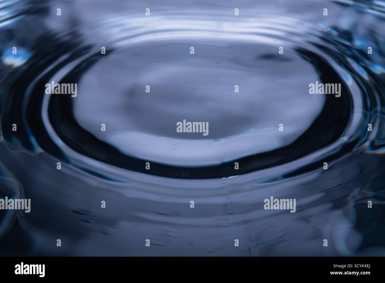309.primo piano della superficie dell'acqua che mostra increspature concentriche dall'impatto centrale. I riflessi e l'illuminazione creano texture e profondità uniformi. Visua astratta Foto Stock