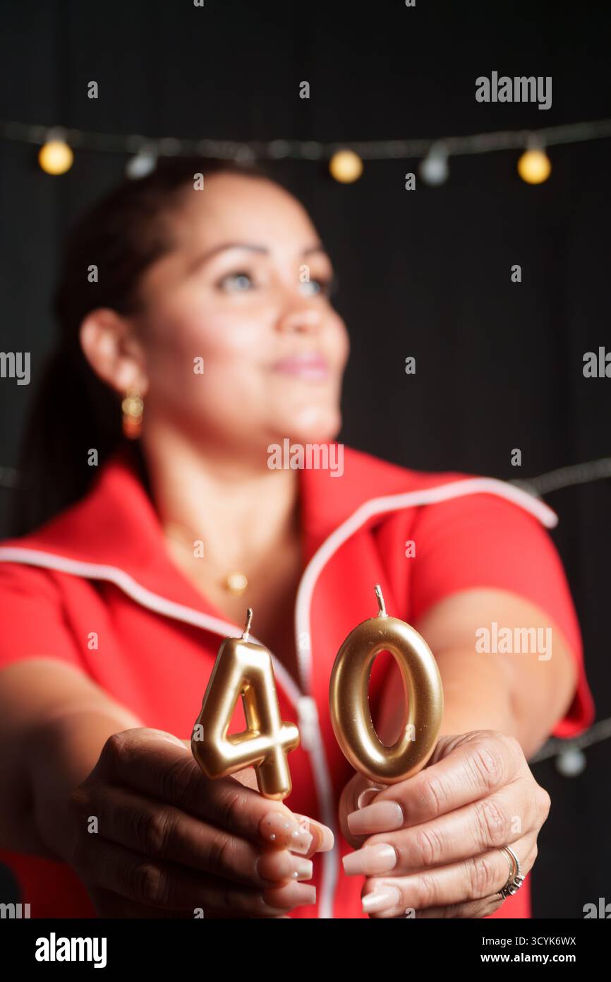 Una donna tiene in mano due candele, una delle quali ha il numero 40. Sta indossando una camicia rossa Foto Stock