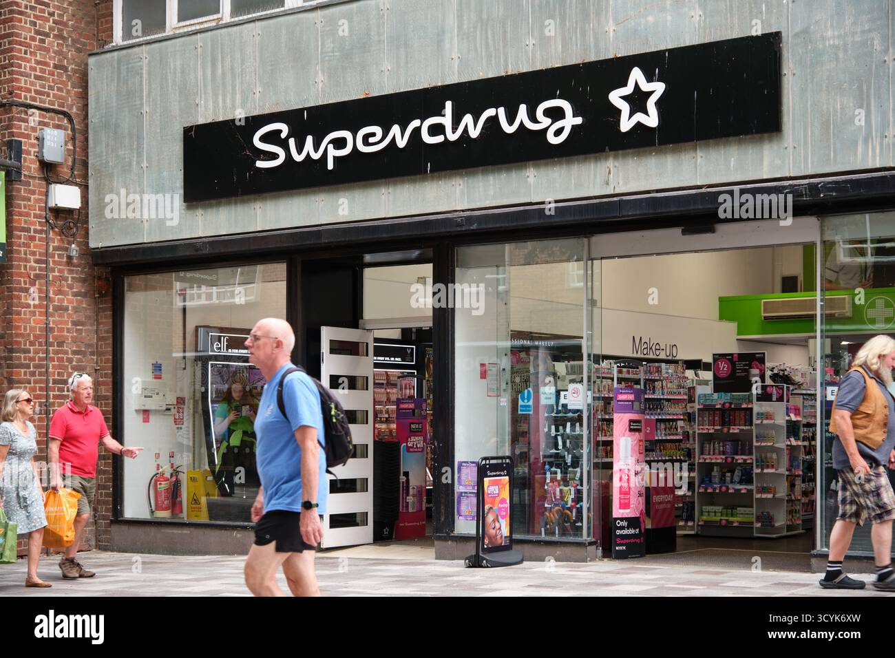 Persone che camminano davanti al negozio di un Superdrug situato in una trafficata strada di Canterbury con mostre visibili all'interno. Canterbury, Kent Foto Stock