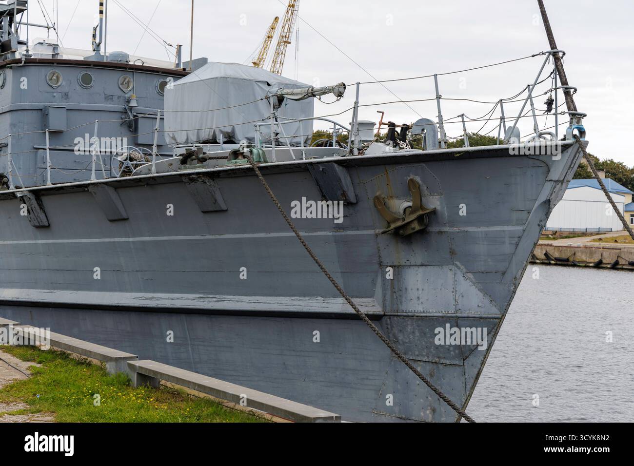 Primo piano della prua e della sovrastruttura anteriore di una grande, vecchia nave militare o pattuglia grigia ormeggiata in un porto, con un'ancora pesante visibile. Foto Stock