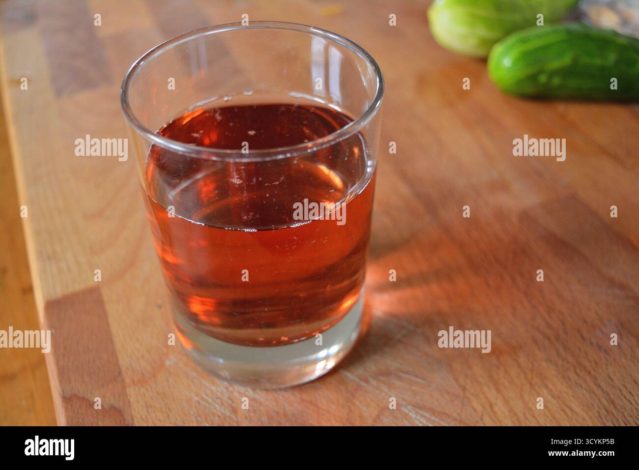 Bicchiere di liquido ambrato trasparente su un tagliere di legno Foto Stock