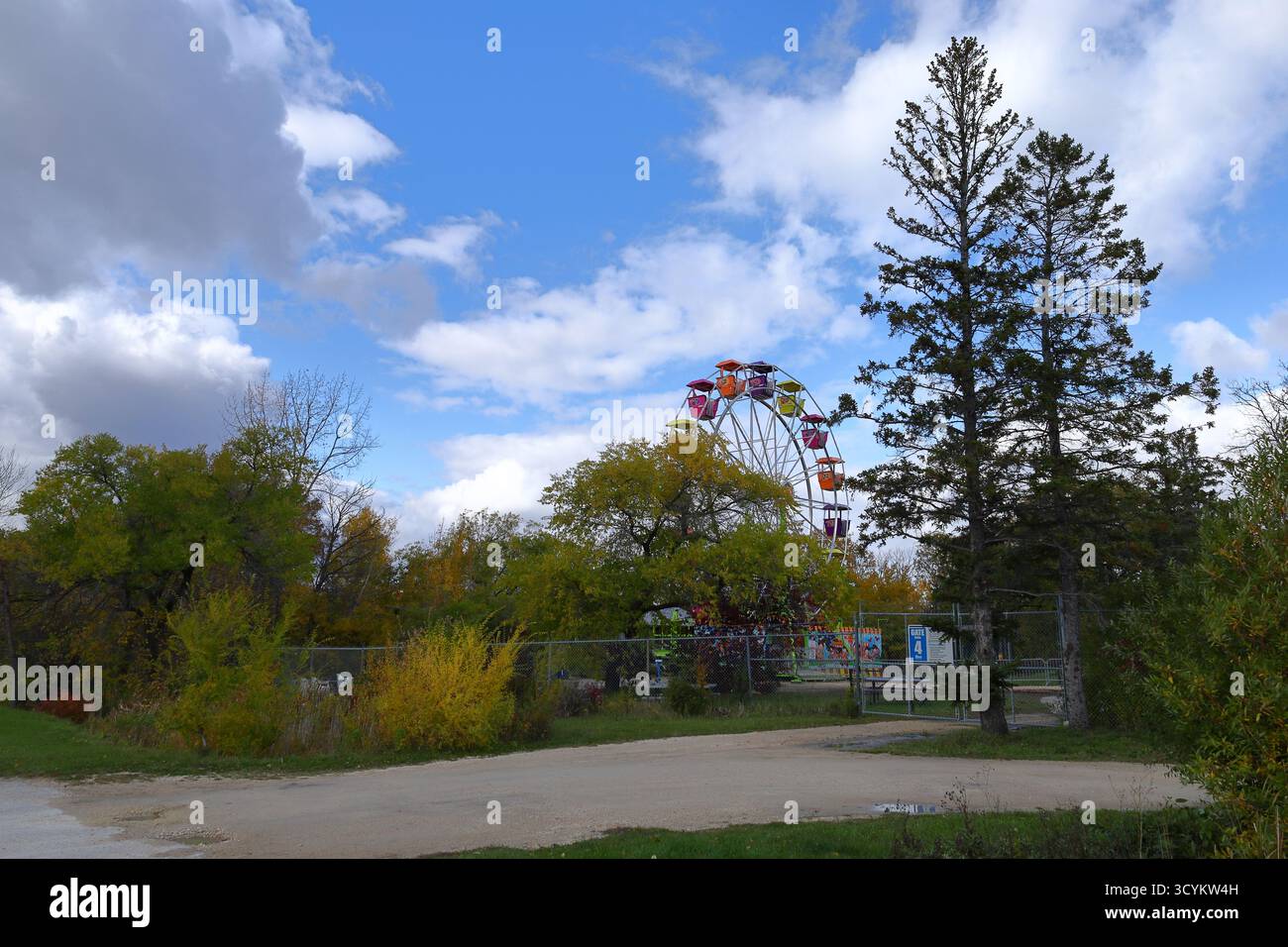 Ruota panoramica colorata sopra gli alberi autunnali. La ruota panoramica luminosa si innalza sopra i colorati alberi autunnali sotto un cielo blu parzialmente nuvoloso negli amusemen dello zoo di Winnipeg Foto Stock