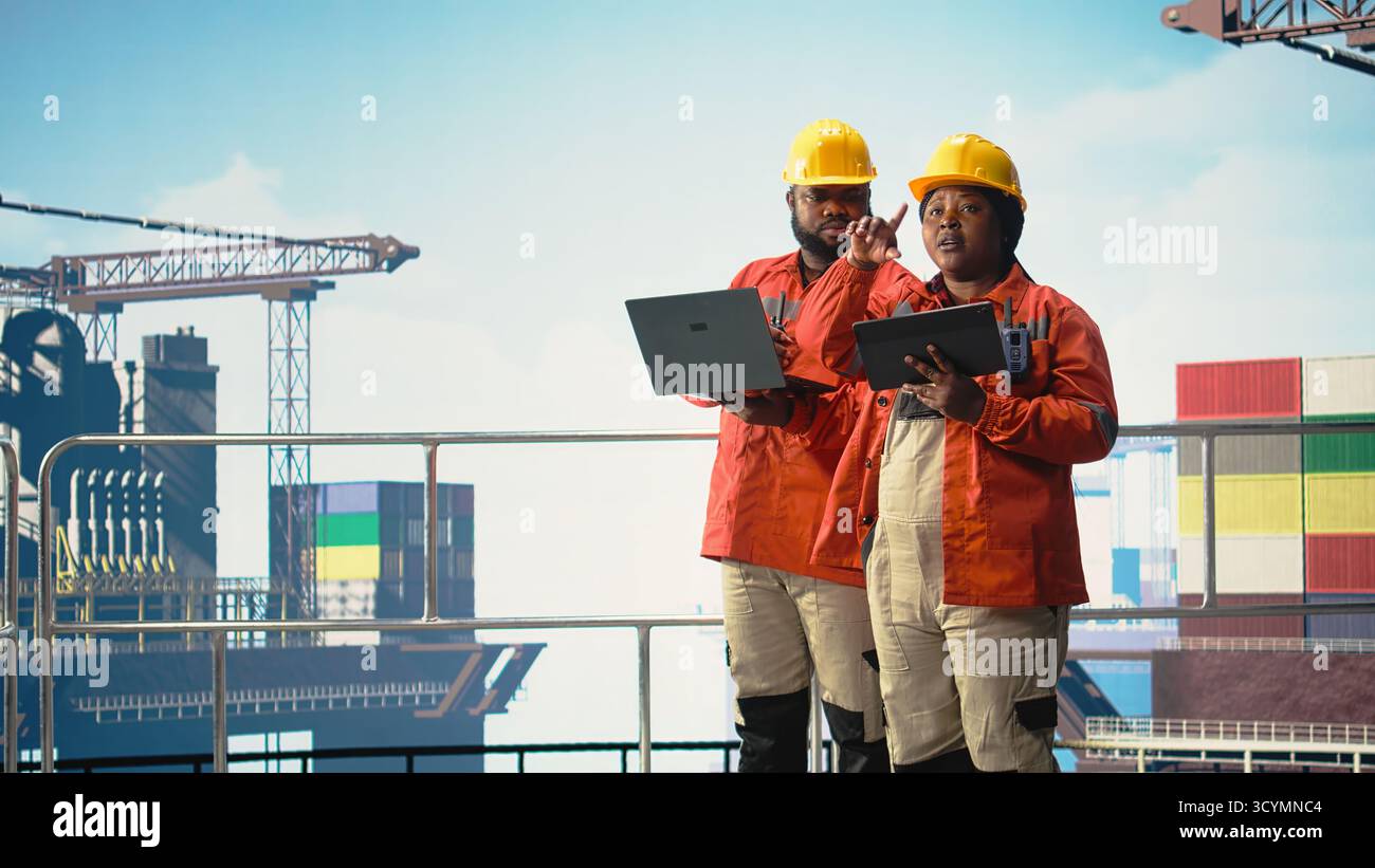 I colleghi della piattaforma offshore supervisionano le operazioni del deck con i dispositivi, garantendo la conformità ai protocolli di sicurezza. Team di tecnici che eseguono il controllo delle attrezzature sui carri di perforazione, Foto Stock