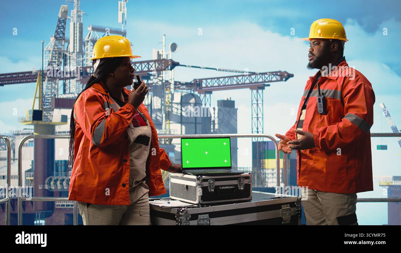 Computer portatile con schermo isolato utilizzato dai colleghi dell'equipaggio del carro di perforazione che tengono in mano un dispositivo radio per monitorare i sistemi. Team di progettazione sul ponte piattaforma offshore utilizzando walkie talkie e notebook Chroma Key, Foto Stock