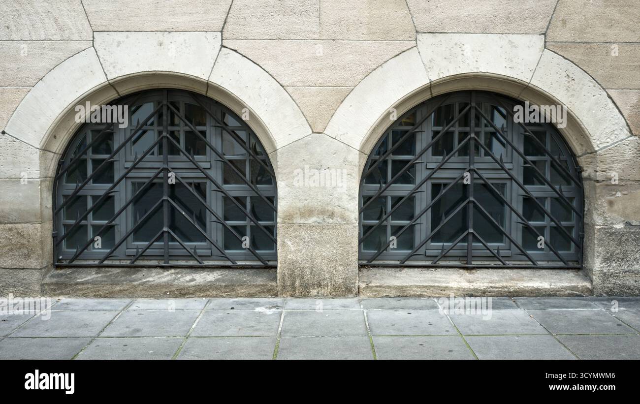 Due finestre ad arco arrotondato al piano inferiore di un vecchio edificio in pietra arenaria, protette da griglie decorative in ferro battuto. Foto Stock