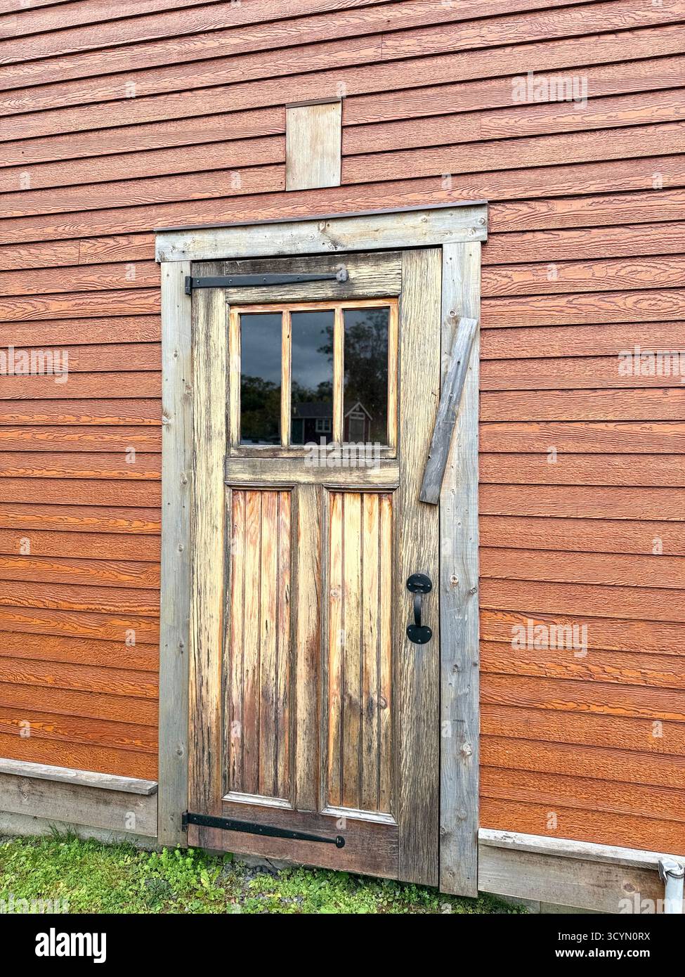 Una vecchia porta di legno sul lato di un rustico edificio in legno. L'edificio e' di colore rosso scuro e la porta e' di colori naturali con tre finestre. Foto Stock