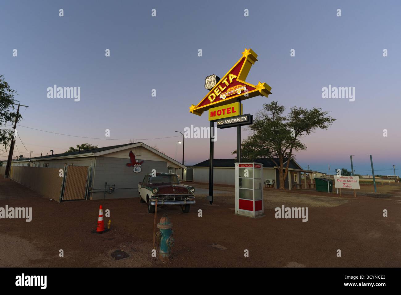 Motel sulla strada con un cartello al neon intempestivo e un'auto arrugginita parcheggiata davanti, evocando la nostalgia americana nel paesaggio desertico del sud-ovest. Foto Stock