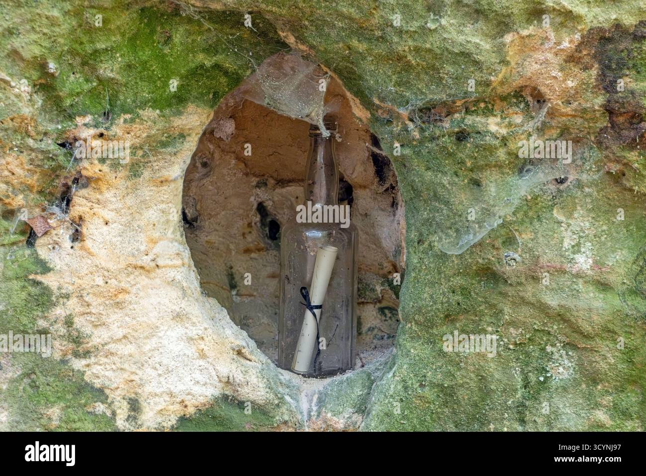 Pergamena arrotolata all'interno di una vecchia bottiglia di vetro posta in un piccolo foro intagliato in una parete di roccia mossy Foto Stock