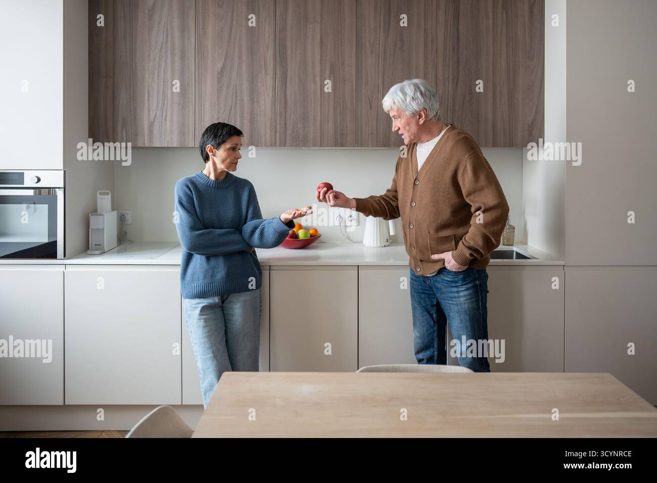 Mela di discordia. La coppia anziana irritata litiga in cucina mentre il marito afferra la frutta, combatte i conflitti Foto Stock