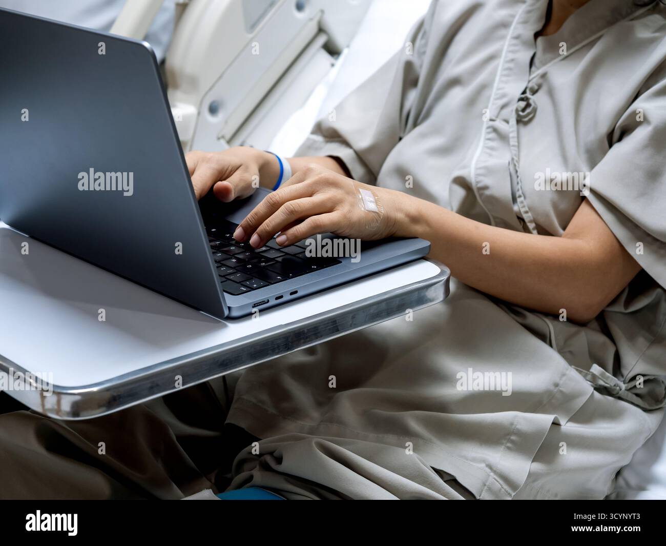 Paziente in ospedale che utilizza un laptop per il lavoro remoto durante il recupero, mostrando il concetto di flessibilità sanitaria, telelavoro e tecnologia digitale Foto Stock