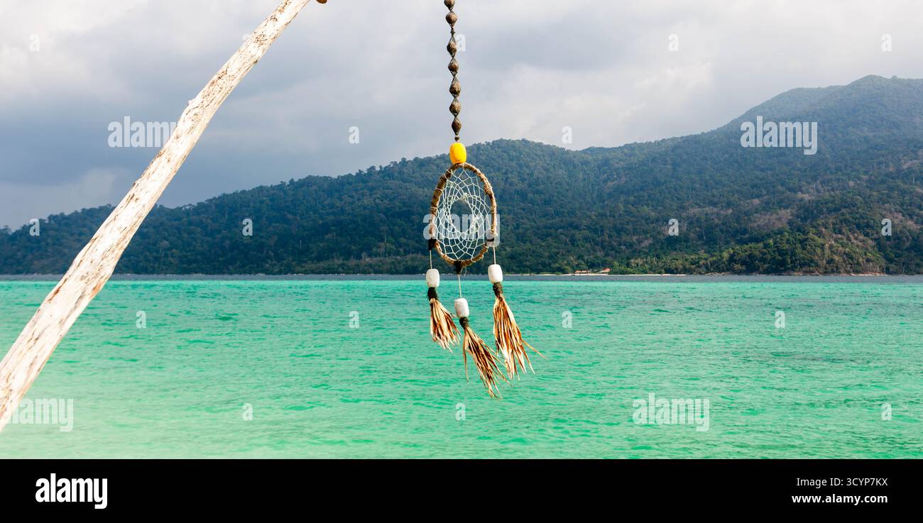 Koh Lipe, Tailandia: Il catcher dei sogni oscilla dolcemente sopra il mare smeraldo, con montagne lussureggianti sotto un cielo limpido. Foto Stock