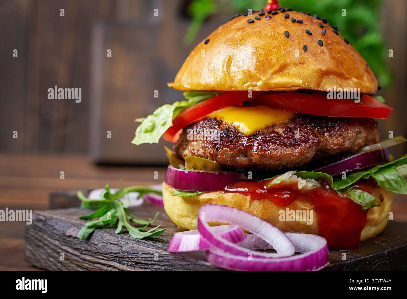 Primo piano di hamburger di manzo con pomodori, formaggio, cetrioli sottaceto, cipolle rosse, lattuga, ketchup e formaggio, su tavola di legno. Foto Stock