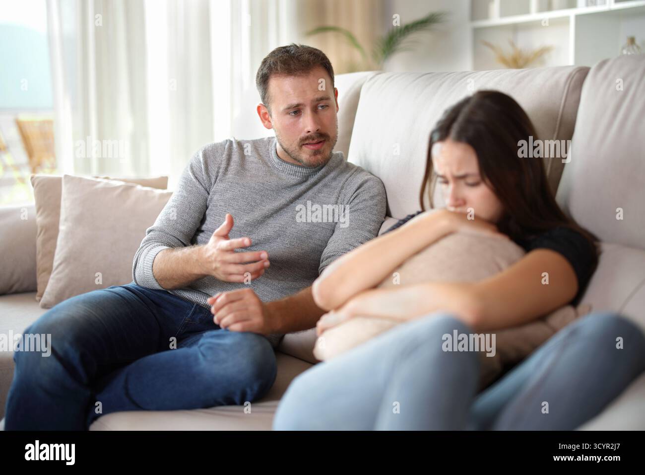 WMAN spiega alla sua triste ragazza seduta su un divano a casa Foto Stock