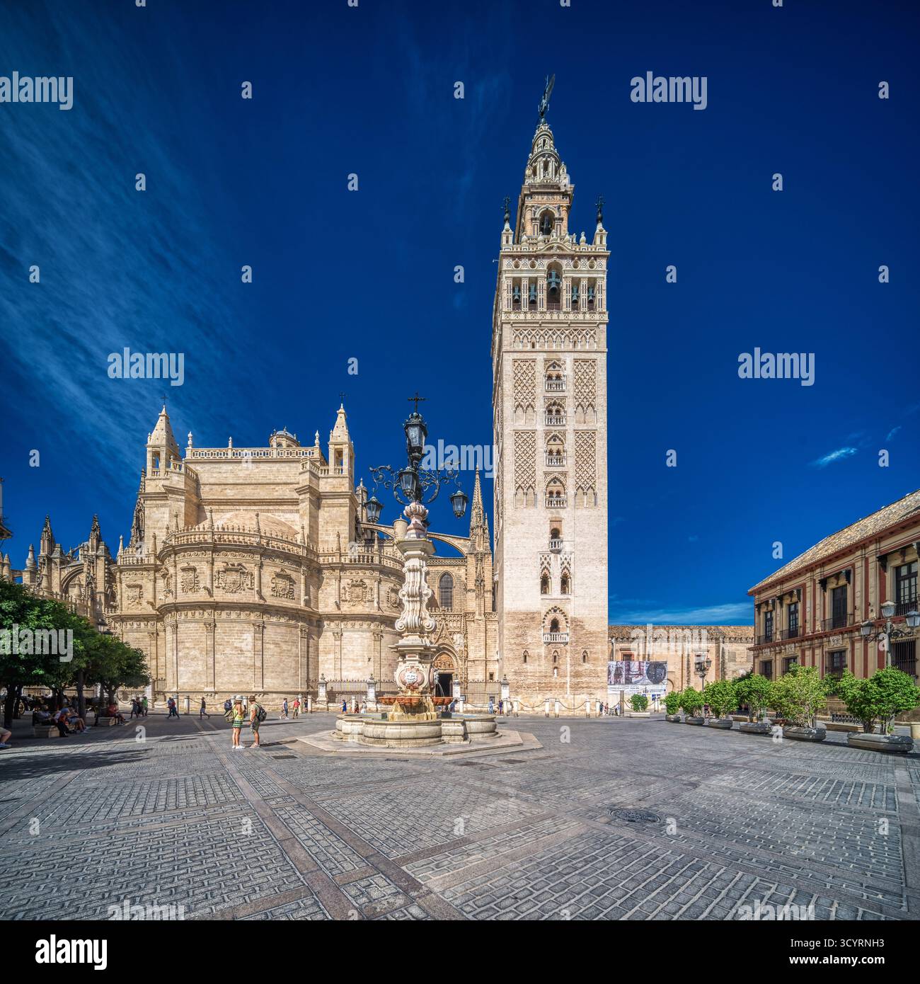 La luce mattutina frizzante mette in evidenza la fontana barocca e il Palazzo dell'Arcivescovo accanto alla torre Giralda in Plaza Virgen de los Reyes, Siviglia, Andalusia. Foto Stock