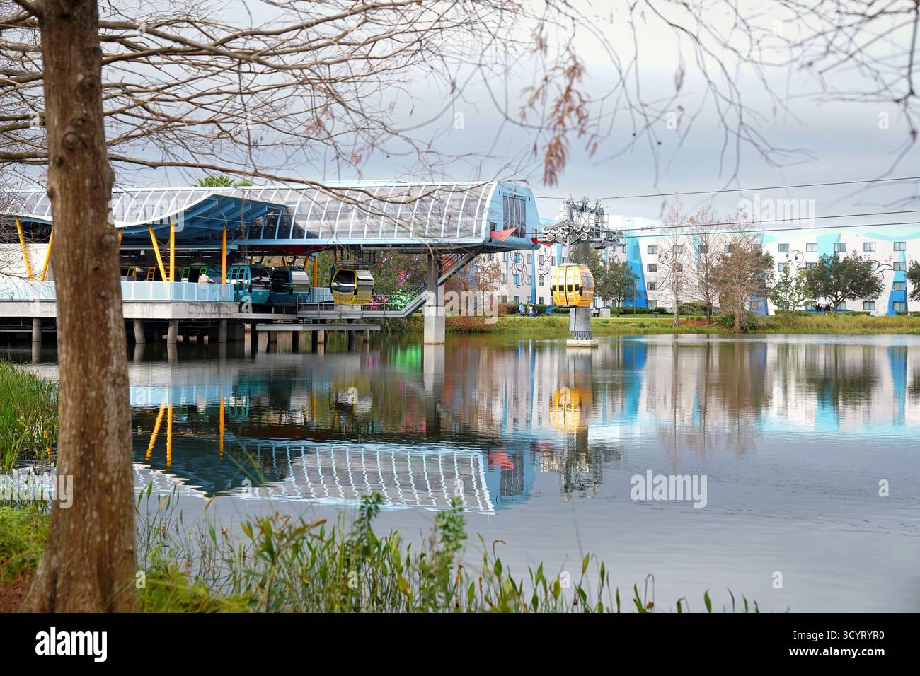 Le gondole Disney Skyliner scivolano sopra un tranquillo lago riflettente vicino all'Art of Animation Resort sotto cieli nuvolosi nell'area del parco a tema di Orlando Foto Stock