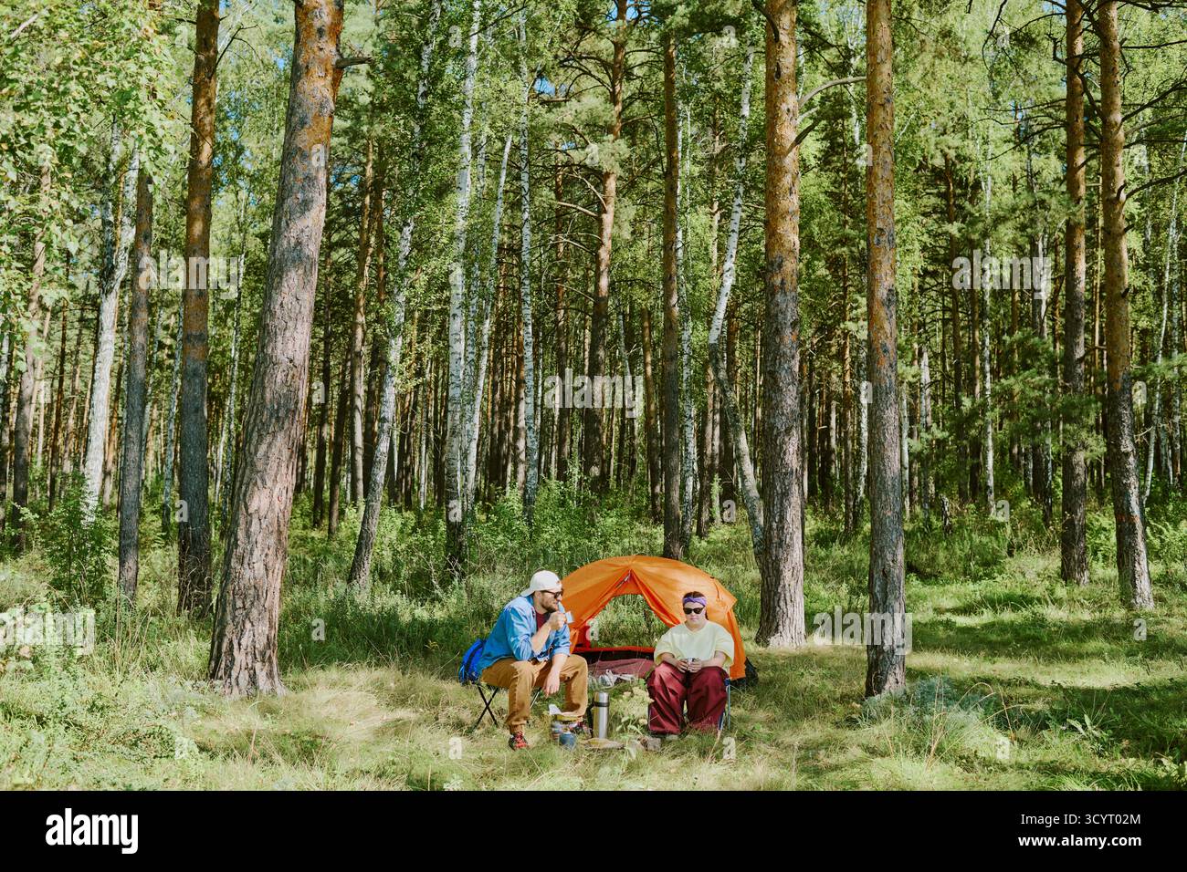Coppia che si rilassa vicino alla tenda mentre cammina nella foresta all'aperto Foto Stock