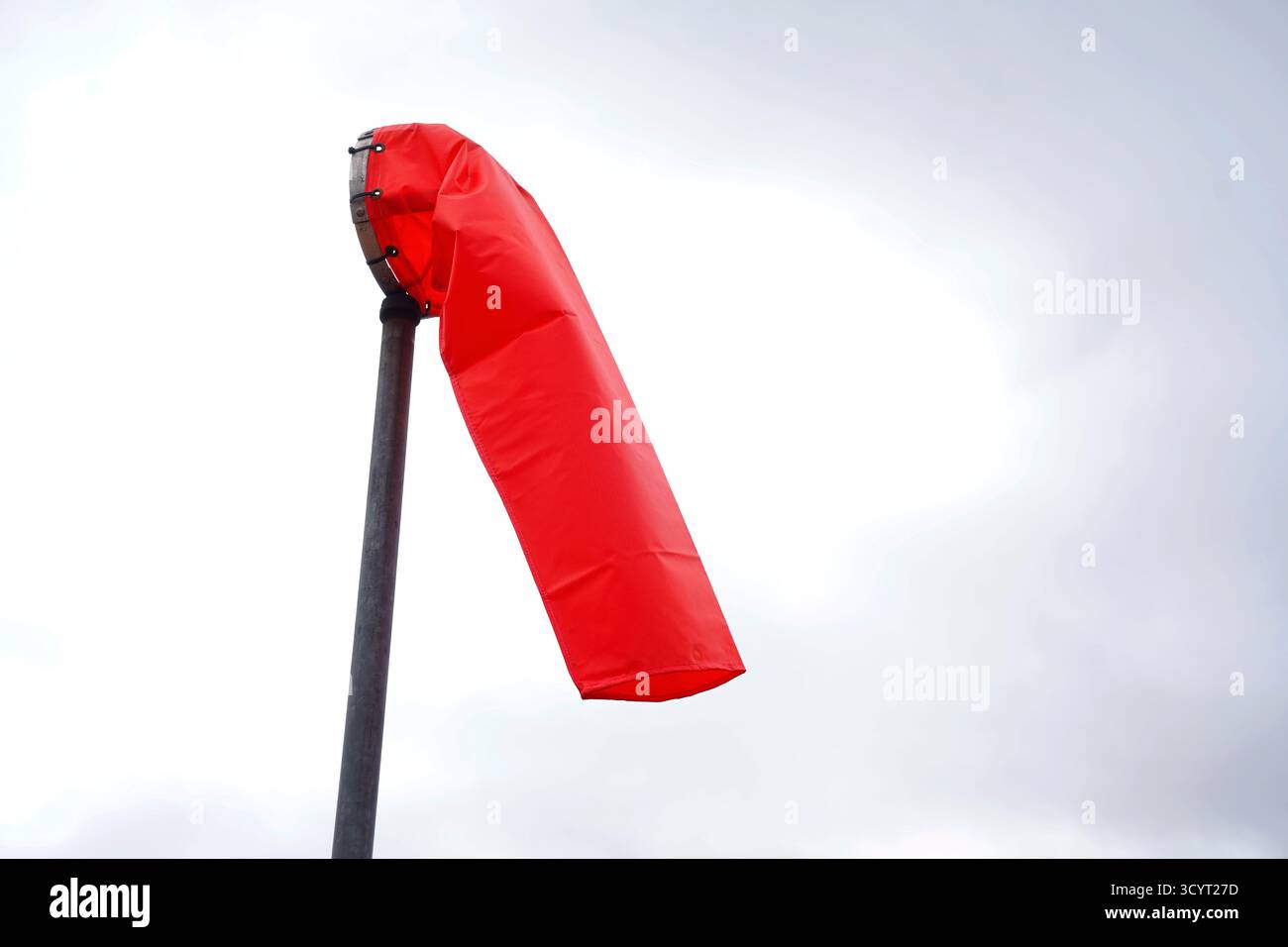 Calza a vento rossa che spicca contro un cielo nuvoloso, simboleggiando la direzione e il movimento a Orlando, Florida Foto Stock