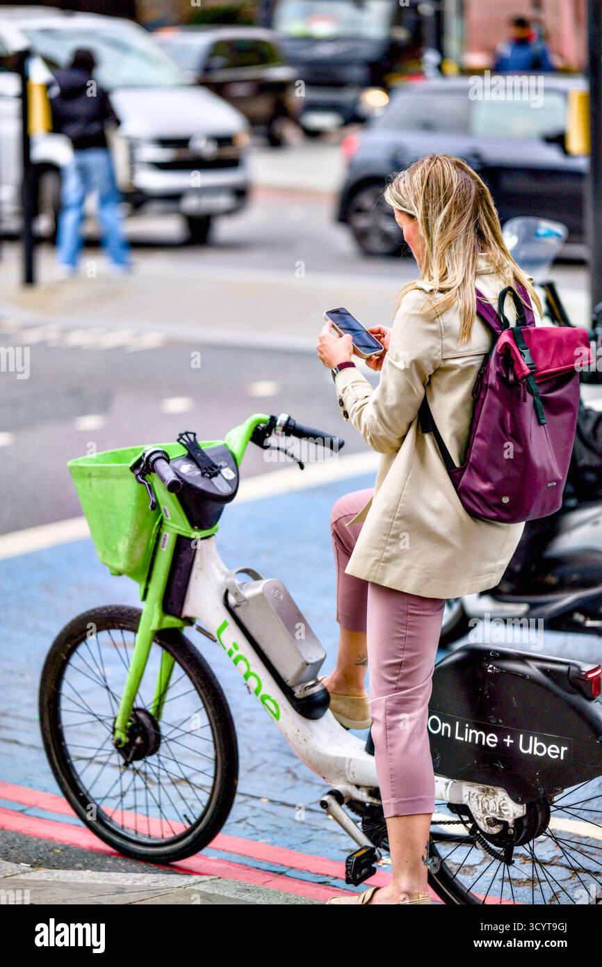 Donna che utilizza il telefono cellulare mentre si ferma al semaforo, Whitechapel High Street, Borough of Tower Hamlets, Londra, Inghilterra, Regno Unito Foto Stock