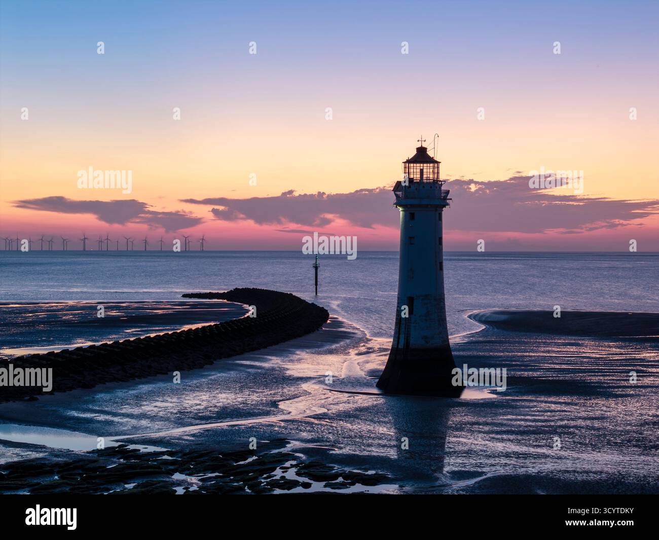 WIRRAL, MERSEYSIDE, INGHILTERRA - 16 AGOSTO 2025: Faro di Perch Rock al tramonto, New Brighton, Wirral, Inghilterra, con una linea di turbine eoliche offshore i Foto Stock