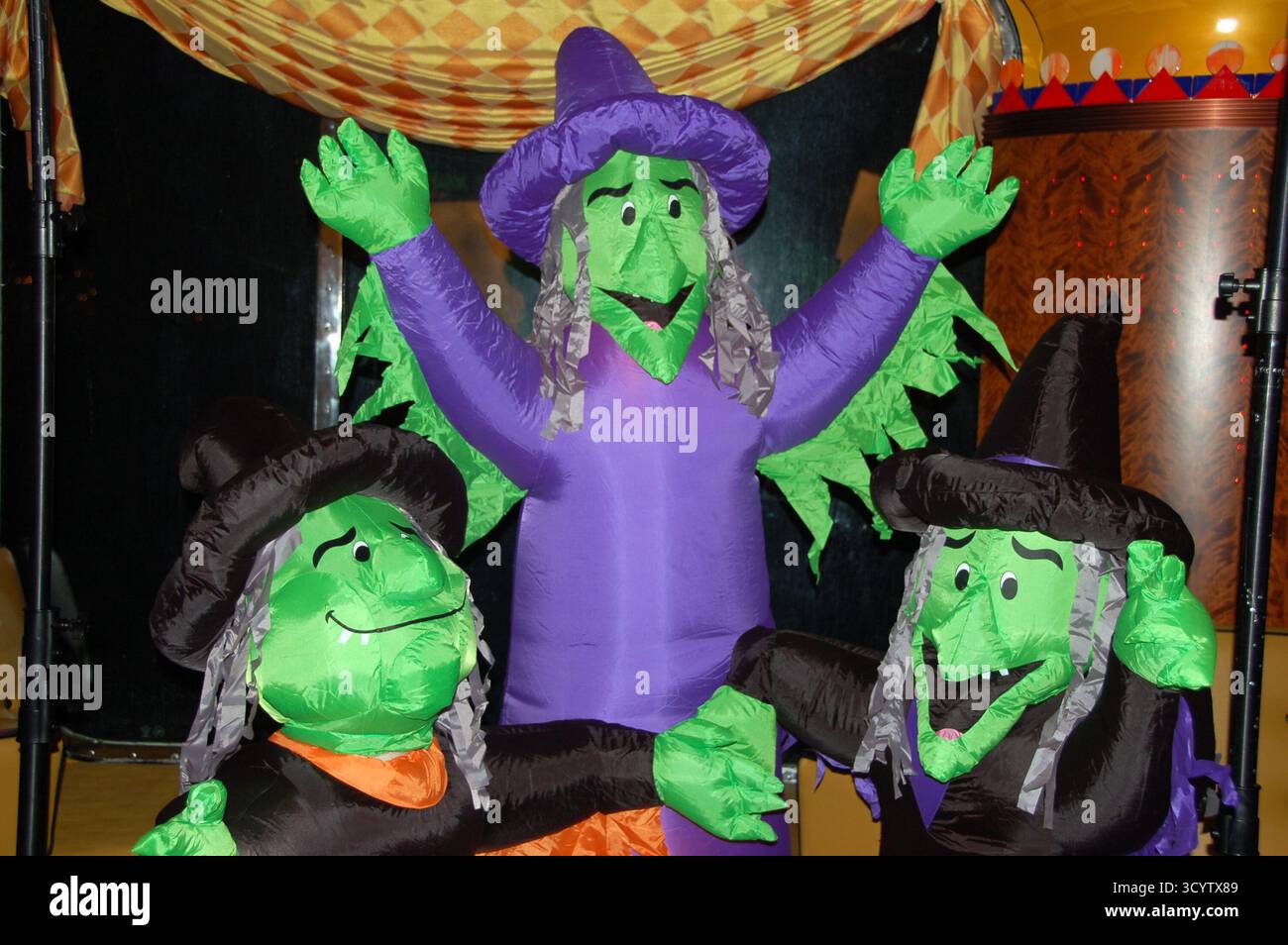 Tre streghe verdi gonfiabili in costumi neri e viola con cappelli, sorridenti e in posa insieme come una divertente decorazione di Halloween all'interno Foto Stock