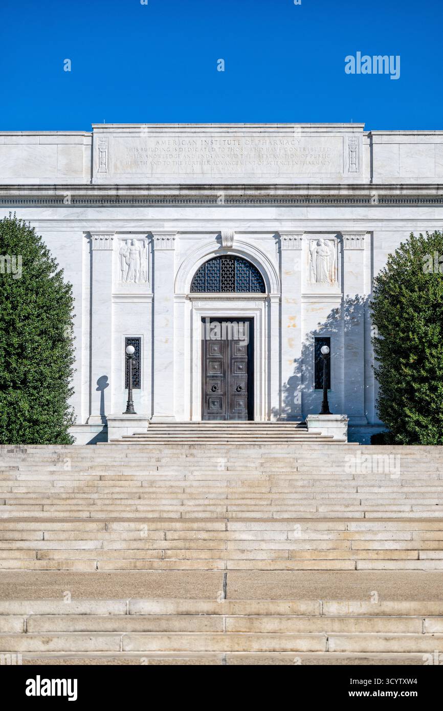 American Institute of Pharmacy Building Washington DC // WASHINGTON DC — The American Institute of Pharmacy Building, una struttura neoclassica progettata da John Russell Pope, è stata dedicata nel 1934. La sua facciata in marmo bianco presenta sculture a rilievo di Leo Friedlander, raffiguranti "PHARMAKEN TEKNE" (Arte della Farmacia) e "PHOS KAI ELPIS" (luce e speranza). Questo National Historic Landmark, noto anche come American Pharmaceutical Association Building, funge da quartier generale dell'American Pharmacists Association (APHA). È dedicato al progresso della sanità pubblica e della scienza farmaceutica. Foto Stock