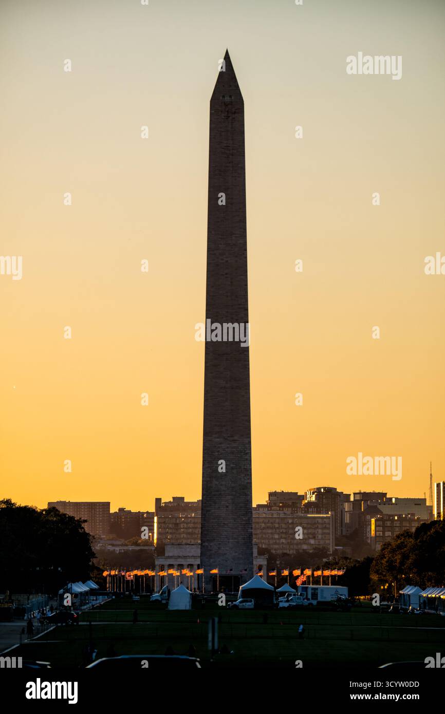 Monumento a Washington presso il Sunrise National Mall Washington DC // WASHINGTON DC - il monumento a Washington sorge contro un cielo all'alba, con bandiere americane alla sua base sul National Mall illuminate dalla luce del mattino. Questo iconico obelisco, costruito in marmo, granito e gneiss di pietra blusa, è un tributo a George Washington. Alto 555 piedi 1/8 pollici (169,294 metri), è un punto di riferimento centrale all'interno del National Mall. Il centro commerciale è un importante parco nazionale all'aperto nel centro di Washington, D.C., che funge da spazio pubblico vitale per eventi e memoriali nazionali. Foto Stock